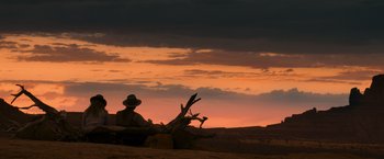 Movie still from “A Million Ways to Die in the West” (2014), directed by Seth MacFarlane – A man sitting on a tree stump in the desert; Extreme Wide shot, Low angle