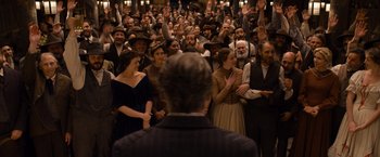 Movie still from “A Million Ways to Die in the West” (2014), directed by Seth MacFarlane – A group of people standing in front of a man in a suit; Wide shot, High angle