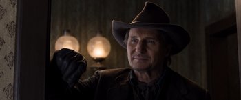 Movie still from “A Million Ways to Die in the West” (2014), directed by Seth MacFarlane – A man wearing a cowboy hat in a dimly - lit room; Close Up shot, Over the shoulder angle