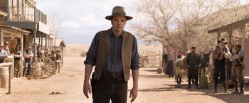 Movie still from “A Million Ways to Die in the West” (2014), directed by Seth MacFarlane – A man wearing a hat and vest standing on a dirt field; Medium shot, Over the shoulder angle