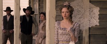 Movie still from “A Million Ways to Die in the West” (2014), directed by Seth MacFarlane – A woman in an old - fashioned dress standing in front of two other women; Medium shot, Over the shoulder angle