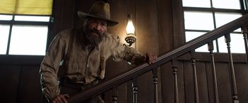 Movie still from “A Million Ways to Die in the West” (2014), directed by Seth MacFarlane – A man with a beard and a hat on leaning on a railing; Medium shot, Low angle