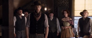Movie still from “A Million Ways to Die in the West” (2014), directed by Seth MacFarlane – A group of people standing in a room; Medium shot, Over the shoulder angle