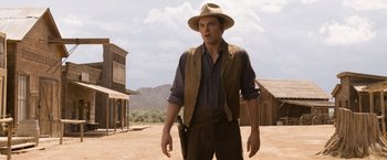 Movie still from “A Million Ways to Die in the West” (2014), directed by Seth MacFarlane – A man in a hat and vest holding a gun; Medium shot, Over the shoulder angle