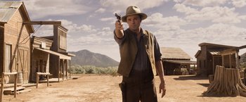 Movie still from “A Million Ways to Die in the West” (2014), directed by Seth MacFarlane – A man holding a gun while standing in a field; Medium shot, Over the shoulder angle