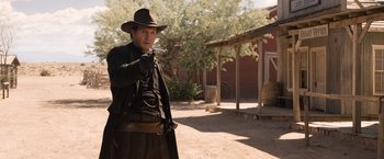 Movie still from “A Million Ways to Die in the West” (2014), directed by Seth MacFarlane – A man holding a gun while wearing a hat; Medium shot, Over the shoulder angle