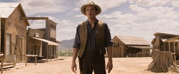 Movie still from “A Million Ways to Die in the West” (2014), directed by Seth MacFarlane – A man wearing a hat standing on a dirt field; Medium shot, Over the shoulder angle