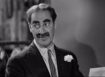 Movie still from “A Night at the Opera” (1935), directed by Sam Wood – A man in a suit and tie wearing glasses; Close Up shot, Over the shoulder angle