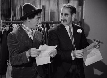 Movie still from “A Night at the Opera” (1935), directed by Sam Wood – A couple of men standing next to each other holding papers; Medium shot, High angle