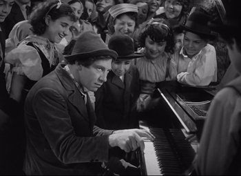 Movie still from “A Night at the Opera” (1935), directed by Sam Wood – A group of people standing next to a man playing a piano; Medium shot, High angle