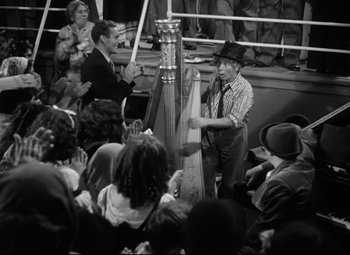 Movie still from “A Night at the Opera” (1935), directed by Sam Wood – A man holding a harp in front of a group of people; Medium shot, High angle