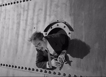 Movie still from “A Night at the Opera” (1935), directed by Sam Wood – A black and white photo of a man looking through a hole in a wall; Medium shot, High angle