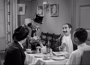 Movie still from “A Night at the Opera” (1935), directed by Sam Wood – A group of people sitting at a table with food; Medium shot, Over the shoulder angle