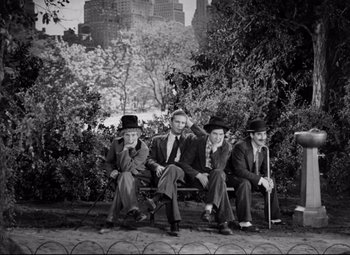 Movie still from “A Night at the Opera” (1935), directed by Sam Wood – A group of men sitting on top of a wooden bench; Wide shot, High angle
