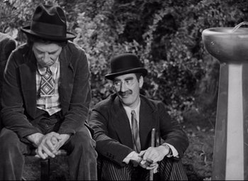 Movie still from “A Night at the Opera” (1935), directed by Sam Wood – Two men in suits and hats sitting next to each other; Medium shot, High angle