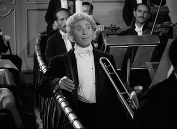 Movie still from “A Night at the Opera” (1935), directed by Sam Wood – An old photo of a man in a tuxedo holding a trombone; Medium shot, Low angle