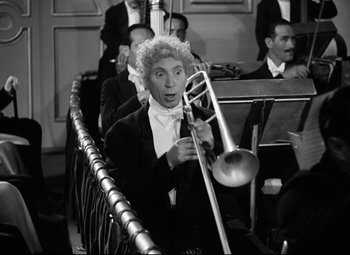 Movie still from “A Night at the Opera” (1935), directed by Sam Wood – A man in a tuxedo holding a trombone in front of a crowd; Medium shot, High angle