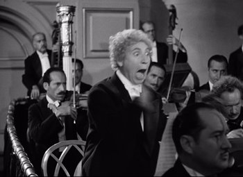 Movie still from “A Night at the Opera” (1935), directed by Sam Wood – An older man in a black suit and white shirt is in front of a group of people; Medium shot, Low angle