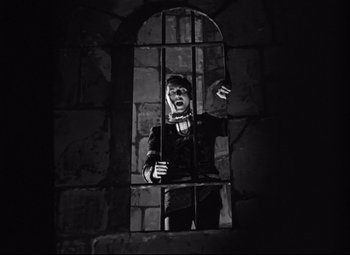 Movie still from “A Night at the Opera” (1935), directed by Sam Wood – A person standing in a cage in a dark room; Wide shot, Low angle