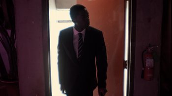 Movie still from “Snowfall” (2017), directed by Hiro Murai – A man wearing a suit and tie standing in a doorway; Medium shot, Low angle