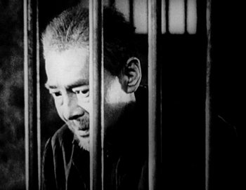 A man in a jail cell looking out of the bars
