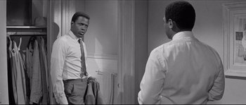 A black and white photo of a man in a suit looking at himself in the mirror