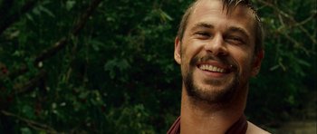 Movie still from “A Perfect Getaway” (2009), directed by David Twohy – A person smiling with trees in the background; Close Up shot, Over the shoulder angle