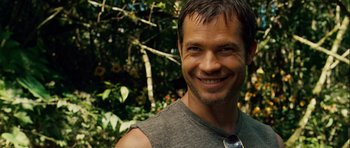 Movie still from “A Perfect Getaway” (2009), directed by David Twohy – A man smiling for the camera in front of a tree; Close Up shot, Over the shoulder angle