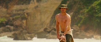 Movie still from “A Perfect Getaway” (2009), directed by David Twohy – A shirtless man holding a frisbee on the beach; Medium shot, Low angle