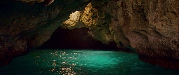 Movie still from “A Perfect Getaway” (2009), directed by David Twohy – A body of water in front of a large cave; Extreme Wide shot, High angle