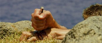 Movie still from “A Perfect Getaway” (2009), directed by David Twohy – A person holding a pen in their hand; Extreme Close Up shot, Overhead angle