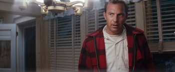 Movie still from “A Perfect World” (1993), directed by Clint Eastwood – A man wearing a red and black jacket standing next to a window; Medium shot, Over the shoulder angle