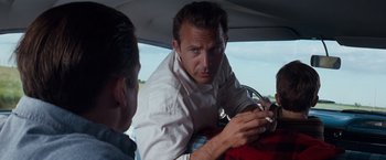 Movie still from “A Perfect World” (1993), directed by Clint Eastwood – A man sitting in the back seat of a car looking at his cell phone; Close Up shot, Over the shoulder angle
