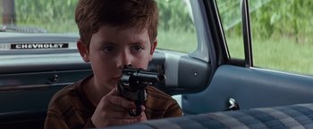 Movie still from “A Perfect World” (1993), directed by Clint Eastwood – A young boy holding a gun in the back seat of a car; Close Up shot, Over the shoulder angle