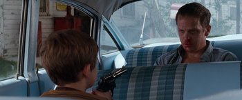 Movie still from “A Perfect World” (1993), directed by Clint Eastwood – A young boy holding a gun in a car seat; Medium shot, Over the shoulder angle