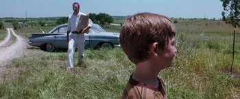Movie still from “A Perfect World” (1993), directed by Clint Eastwood – A man and a boy in a field with a car in the background; Medium shot, Over the shoulder angle