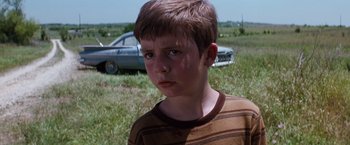 Movie still from “A Perfect World” (1993), directed by Clint Eastwood – A young boy standing in the grass next to a car; Close Up shot, Low angle