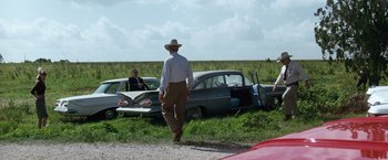Movie still from “A Perfect World” (1993), directed by Clint Eastwood – A man walking in front of two old cars in a field; Wide shot, Over the shoulder angle