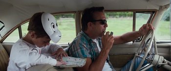 Movie still from “A Perfect World” (1993), directed by Clint Eastwood – A man sitting in the back seat of a car with a mask on; Medium shot, Over the shoulder angle