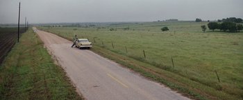 Movie still from “A Perfect World” (1993), directed by Clint Eastwood – A man standing on the side of a road next to a car; Extreme Wide shot, High angle