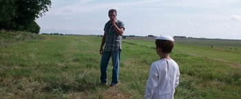 Movie still from “A Perfect World” (1993), directed by Clint Eastwood – A man standing in a grassy field with a boy; Wide shot, Over the shoulder angle
