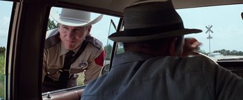 Movie still from “A Perfect World” (1993), directed by Clint Eastwood – A man in a cowboy hat is sitting in the drivers seat of a car; Medium shot, Over the shoulder angle