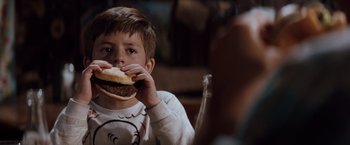 Movie still from “A Perfect World” (1993), directed by Clint Eastwood – A young boy is eating a hamburger at a table; Close Up shot, Over the shoulder angle