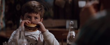 Movie still from “A Perfect World” (1993), directed by Clint Eastwood – A young boy eating a hamburger at a table; Close Up shot, Over the shoulder angle