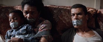Movie still from “A Perfect World” (1993), directed by Clint Eastwood – Two people sitting on a couch with duct tape over their mouths; Close Up shot, High angle