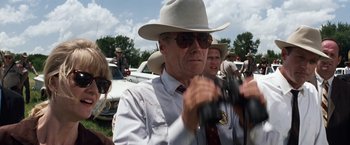Movie still from “A Perfect World” (1993), directed by Clint Eastwood – A man in a cowboy hat holding a pair of binoculars in front of a crowd; Close Up shot, Over the shoulder angle