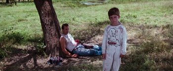Movie still from “A Perfect World” (1993), directed by Clint Eastwood – A man and a boy sitting next to a tree; Medium shot, Low angle