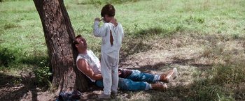 Movie still from “A Perfect World” (1993), directed by Clint Eastwood – A man and a boy sitting on the ground next to a tree; Wide shot, Low angle