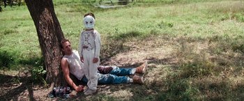 Movie still from “A Perfect World” (1993), directed by Clint Eastwood – A person laying on the ground next to a child wearing a mask; Medium shot, High angle