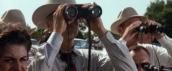 Movie still from “A Perfect World” (1993), directed by Clint Eastwood – A man looking through a pair of binoculars while wearing a hat; Close Up shot, Low angle